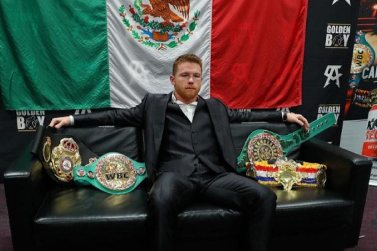 De terno e com a bandeira do México ao fundo, Canelo posa com seus cinturões