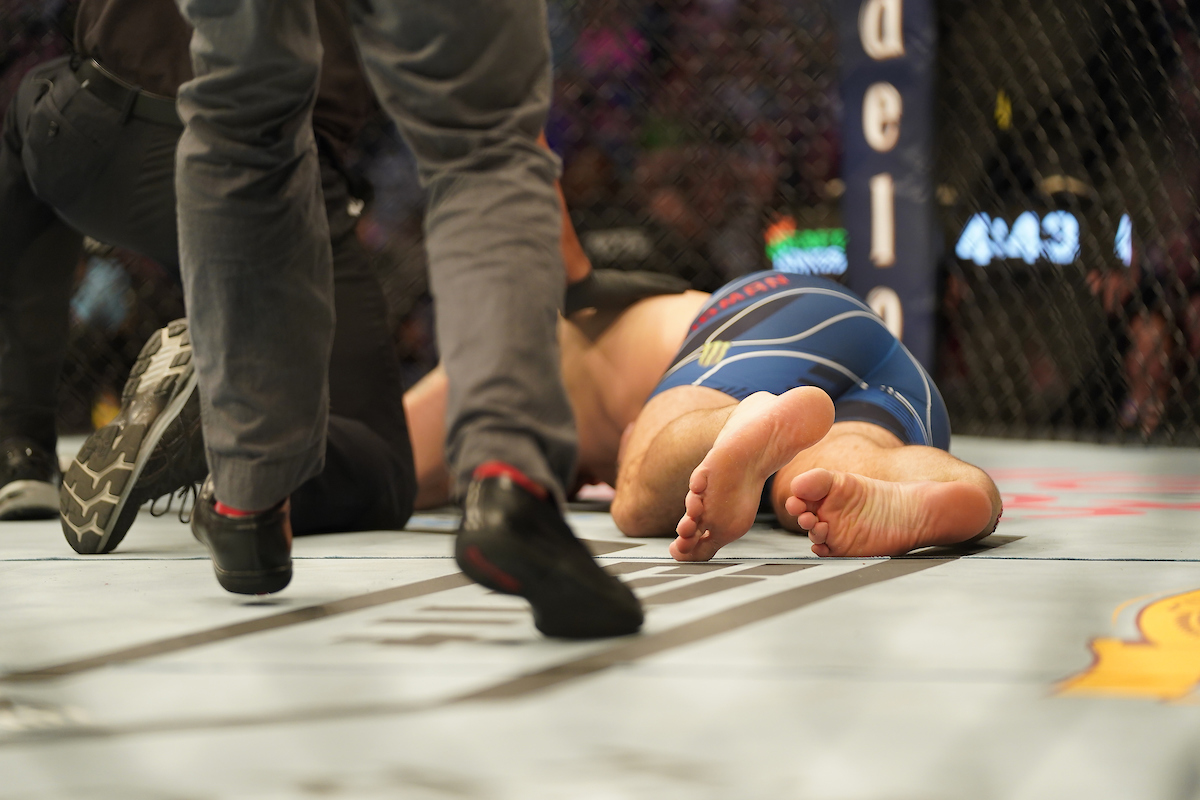 Chris Weidman deitado no octógono após ter fraturado a perna em luta contra Uriah Hall no UFC 261.