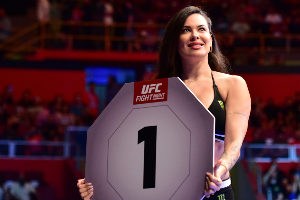 Camila Oliveira segura a placa indicando o round 1 de uma luta do UFC SP