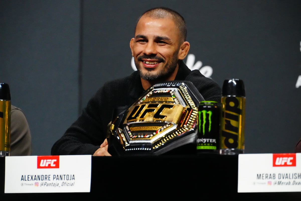 Alexandre Pantoja sorri ao lado do cinturão na coletiva do UFC 323
